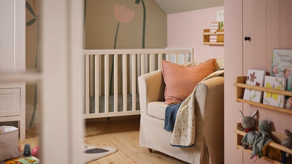 A TULLSTA armchair with a Lofallet beige cover, a GULDVÄVARE blanket and a cushion in a pink cover on it, by a SUNDVIK cot.
