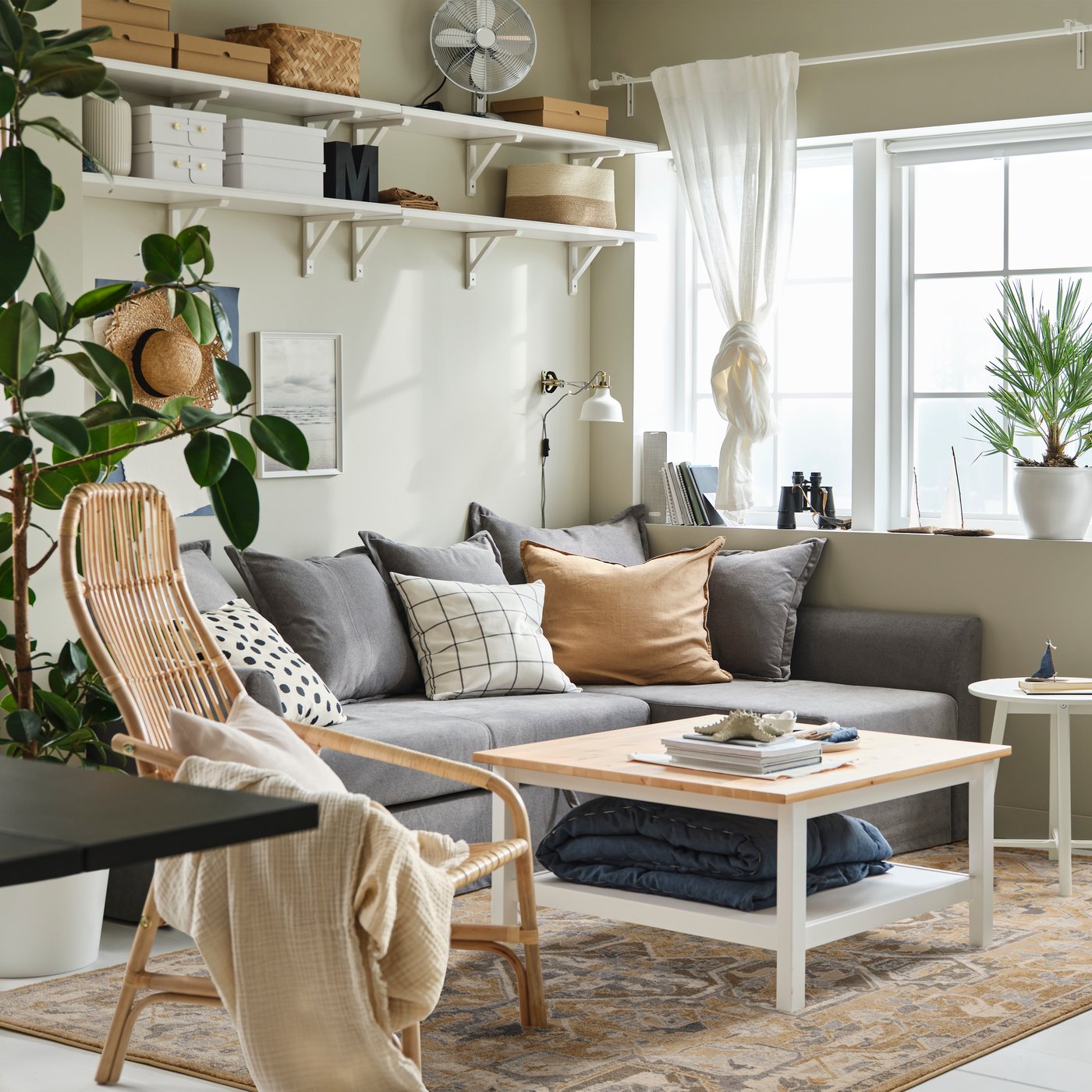 Ein großer, beiger JÄRNVÄG Teppich mit orientalischem Muster liegt unter einem grauen Ecksofa. Der Rest des Zimmers ist hell eingerichtet - mit vielen Pflanzen und natürlichen Materialien.