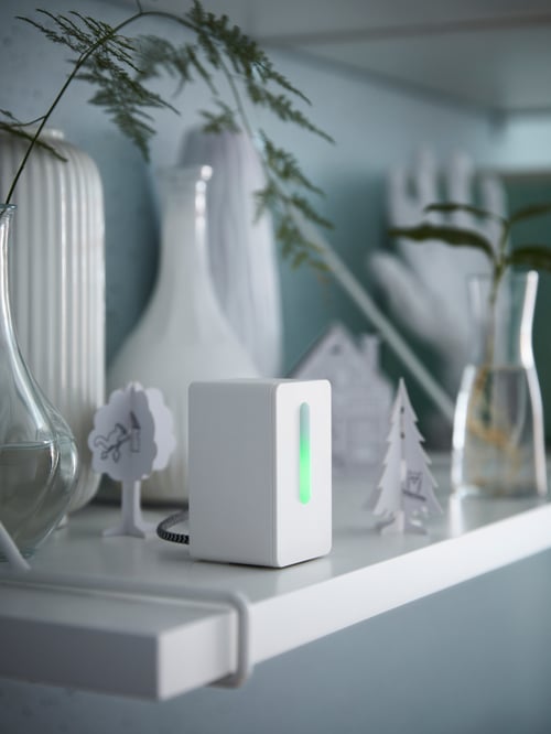 Close-up of a white air quality sensor, multiple vases, and multiple decorative items on a white shelf.