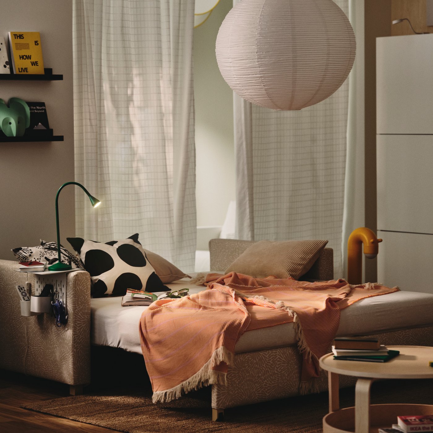 En klart orange/rosa LAPPKATTFOT pläd i vardagsrummet på en utbäddad beige bäddsoffa.