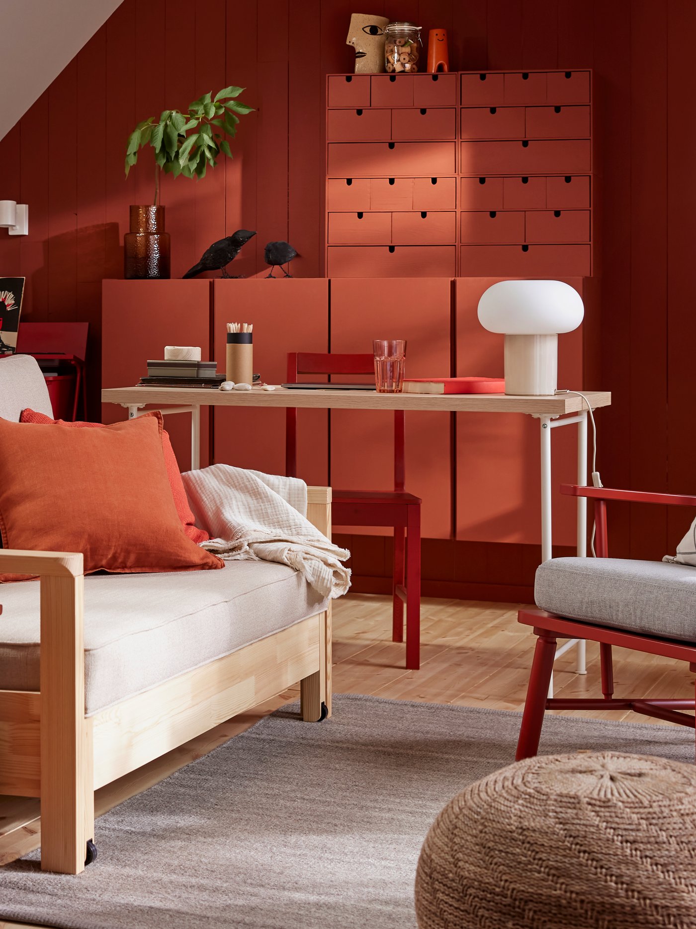 Un canapé-lit TORNSBORG trône dans une salle familiale avec un tapis gris TIDTABELL et un meuble de rangement en pin peint en rouge.