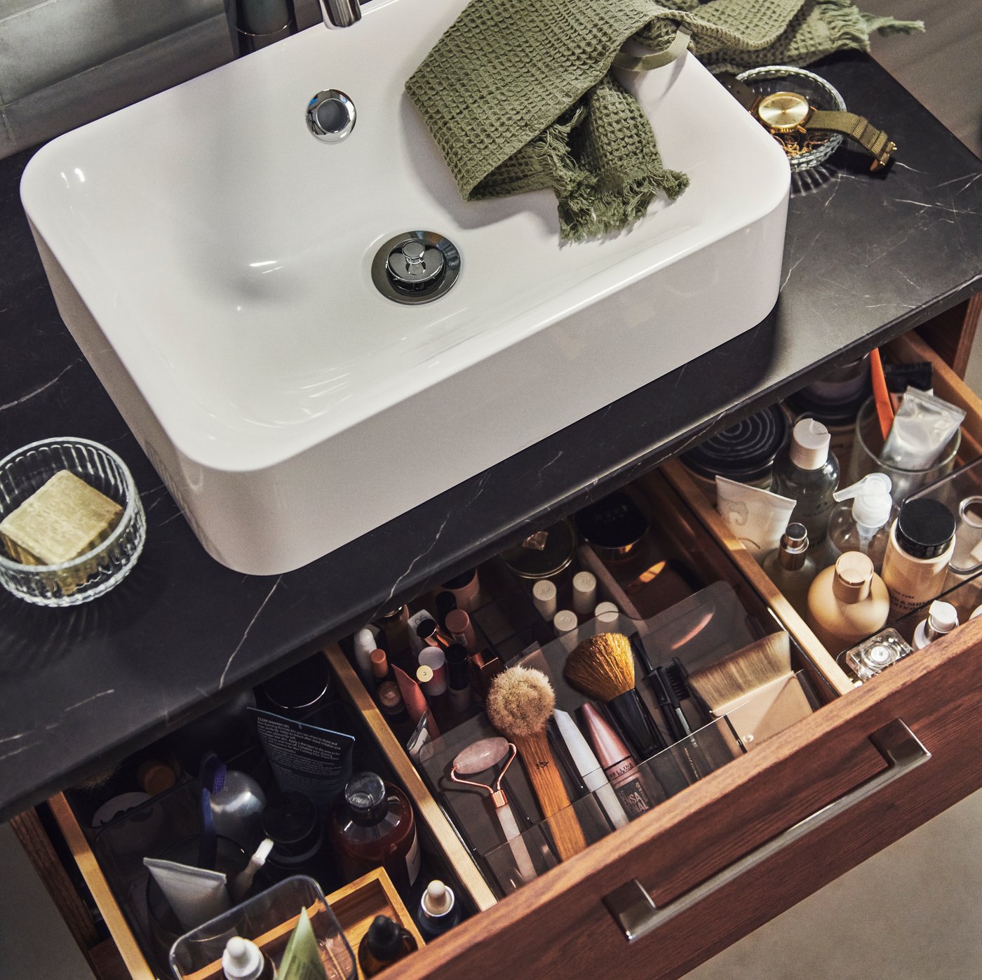 A HÖRVIK wash-basin on top of a wash-stand with one drawer pulled out, showing makeup and accessories organised inside.