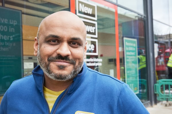 A co-worker wearing a blue sweater with a nametag smiles at the camera.
