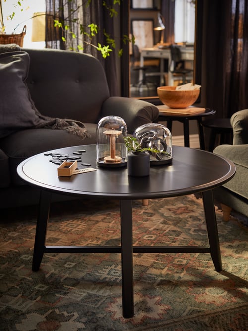 Wohnzimmer mit einem KRAGSTA Couchtisch auf einem VESTERVIG Teppich, u. a. mit einem ESSEBODA 2er-Sofa, einem ESSEBODA 3er-Sofa, einem EVALI Plaid und zwei SKÖNJA Glasglocken mit Tellern.