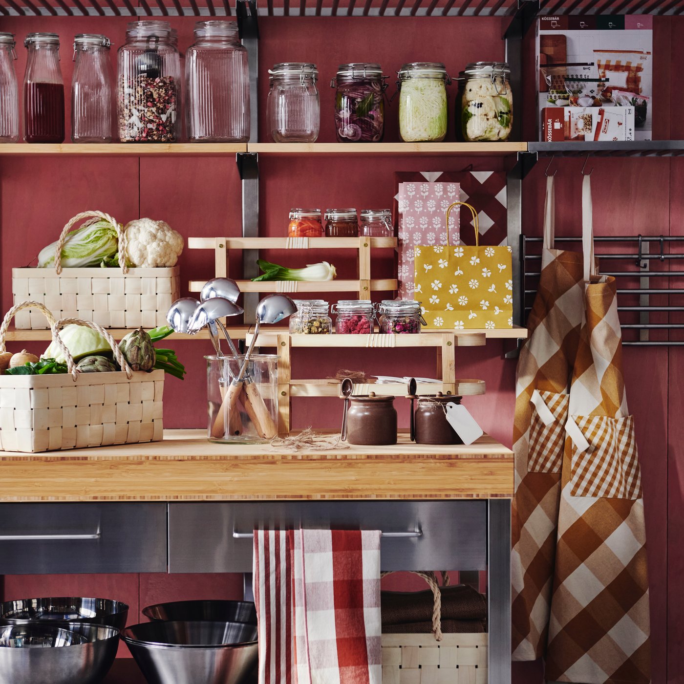 A kitchen with shelves and a table adorned with several KÖSSEBÄR items, like baskets, jars, tea towels, aprons, and more.