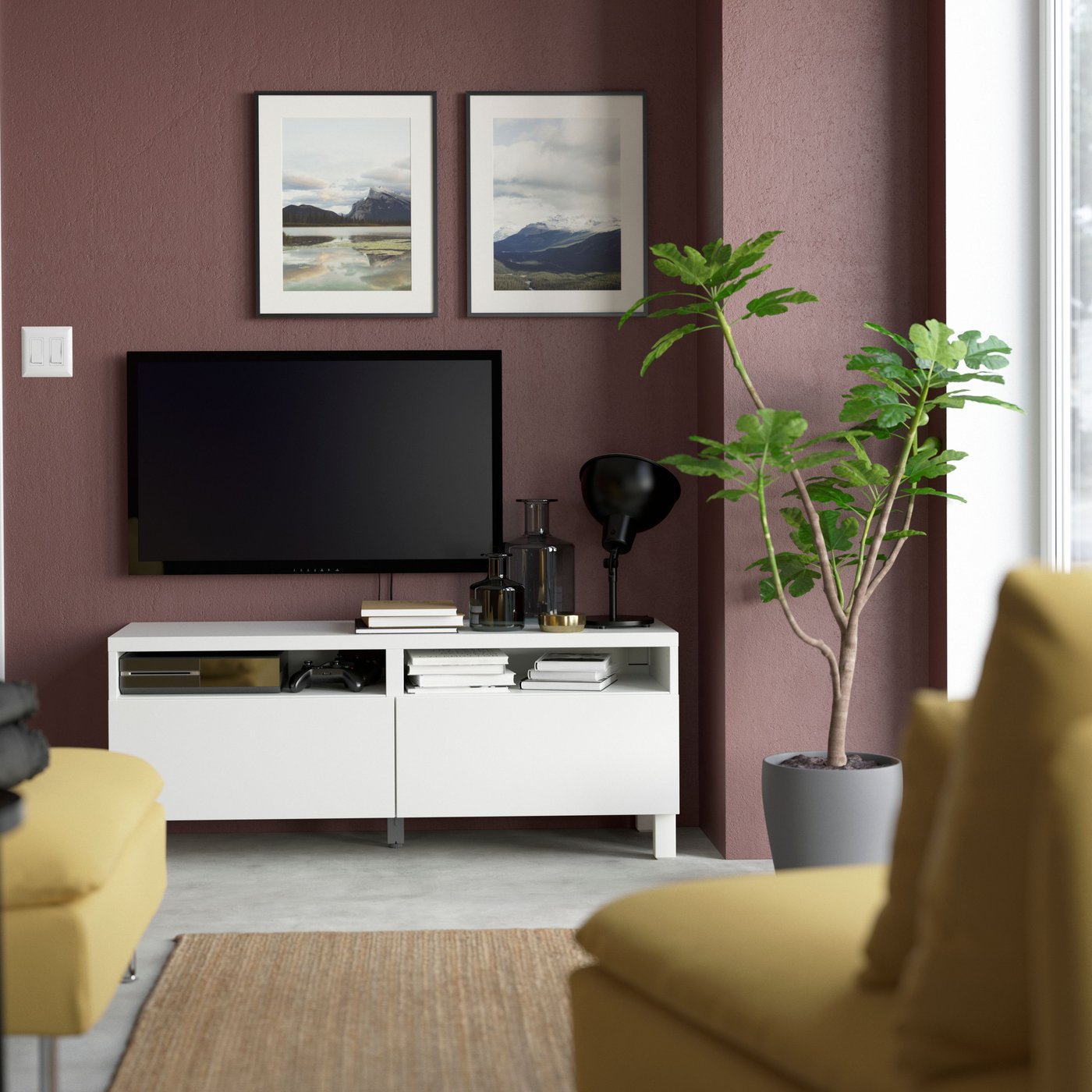 A BESTÅ TV bench with drawers stands underneath a wall-mounted TV screen and two paintings of landscapes.