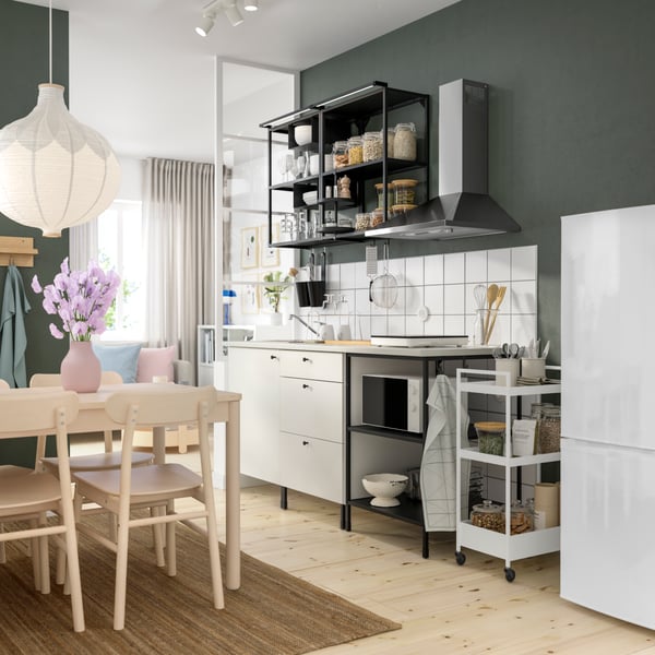 A small ENHET kitchen with white cabinets and open black storage above and beside. Small white utility cart beside 