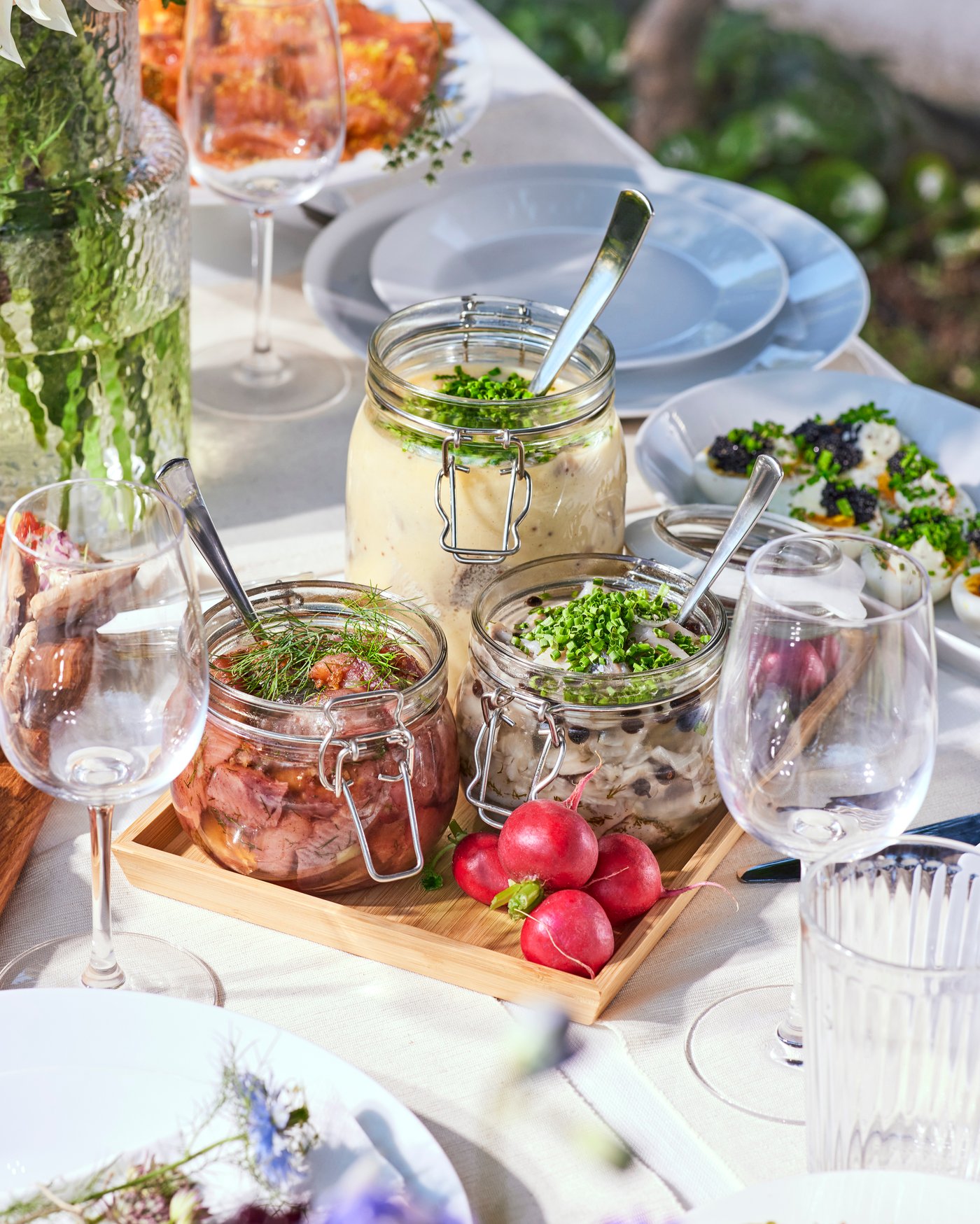 A table set with a midsummer lunch of herring served in glass jars.