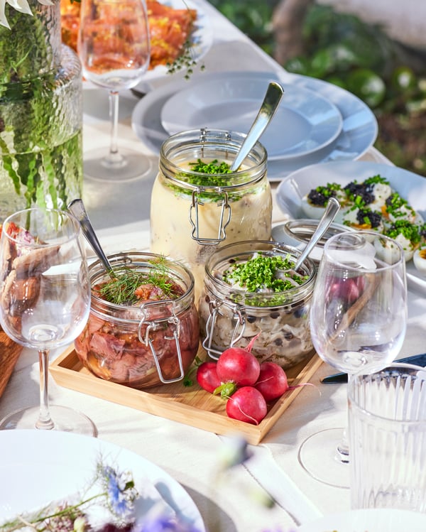 A table set with a midsummer lunch of herring served in glass jars.