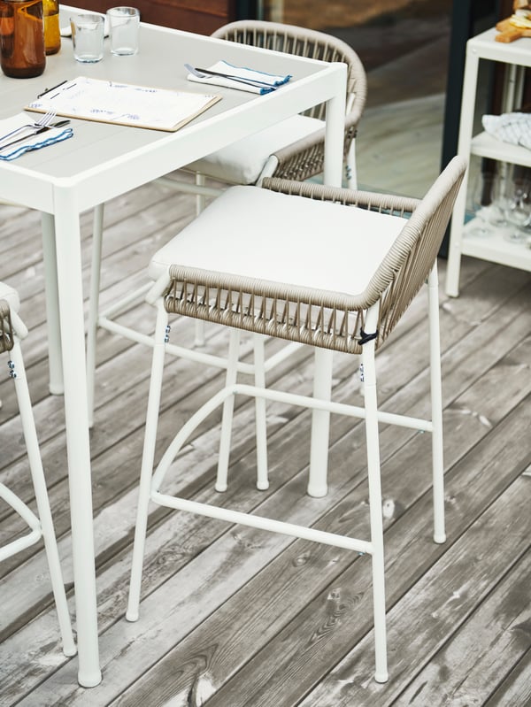 Three SEGERÖN bar stools are standing around a SEGERÖN bar table on the wooden deck of an outdoor restaurant.