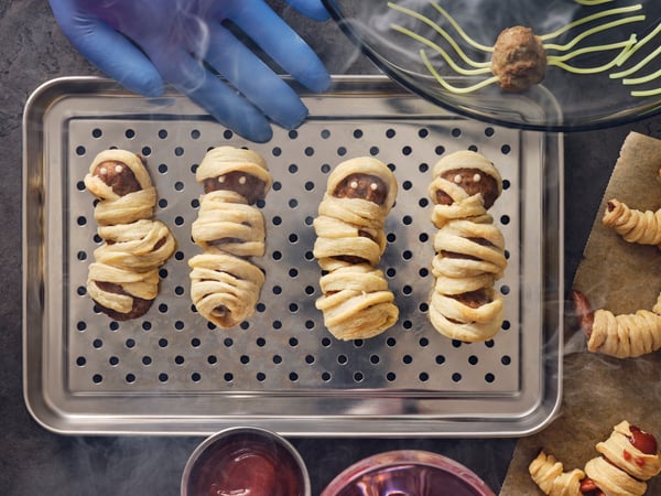 Four meatball mummies made with HUVUDROLL plant balls or meatballs and puffed pastry strips on a stainless steel dish.