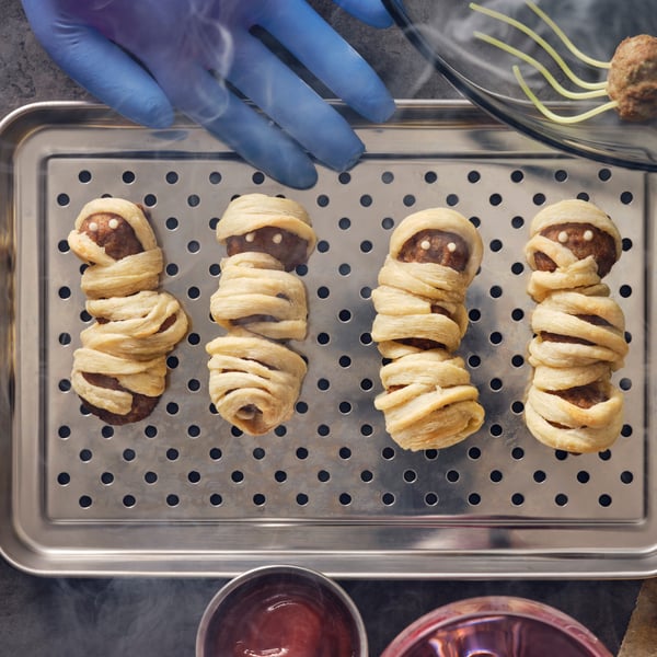 Trois boulettes-momies faites de boulettes végétales ou à la viande HUVUDROLL et de lanières de pâte feuilletée sur un plat en acier inoxydable.