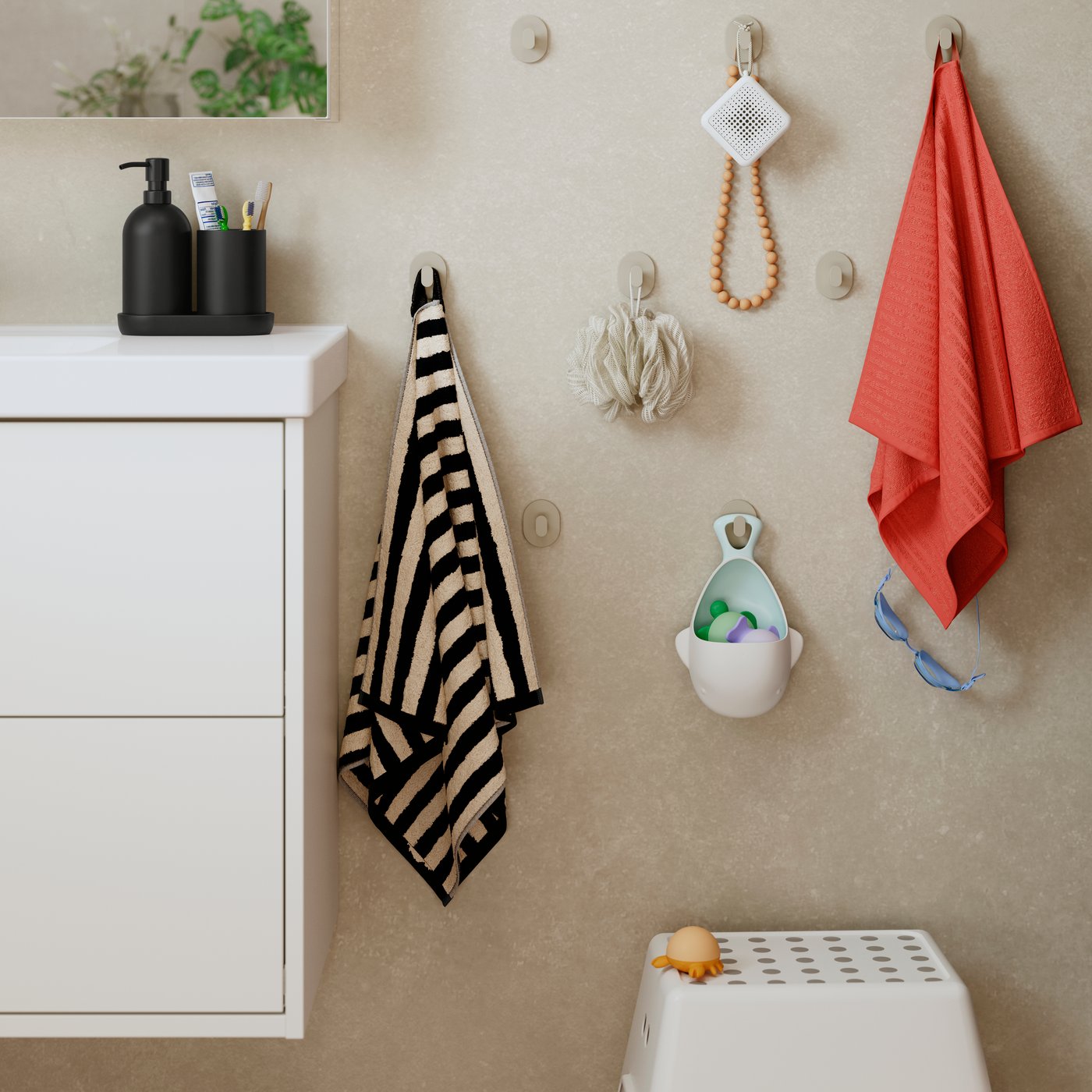 A bathroom setting features several beige FLORSJÖN hooks on the wall holding a striped towel and toys next to a storage unit.
