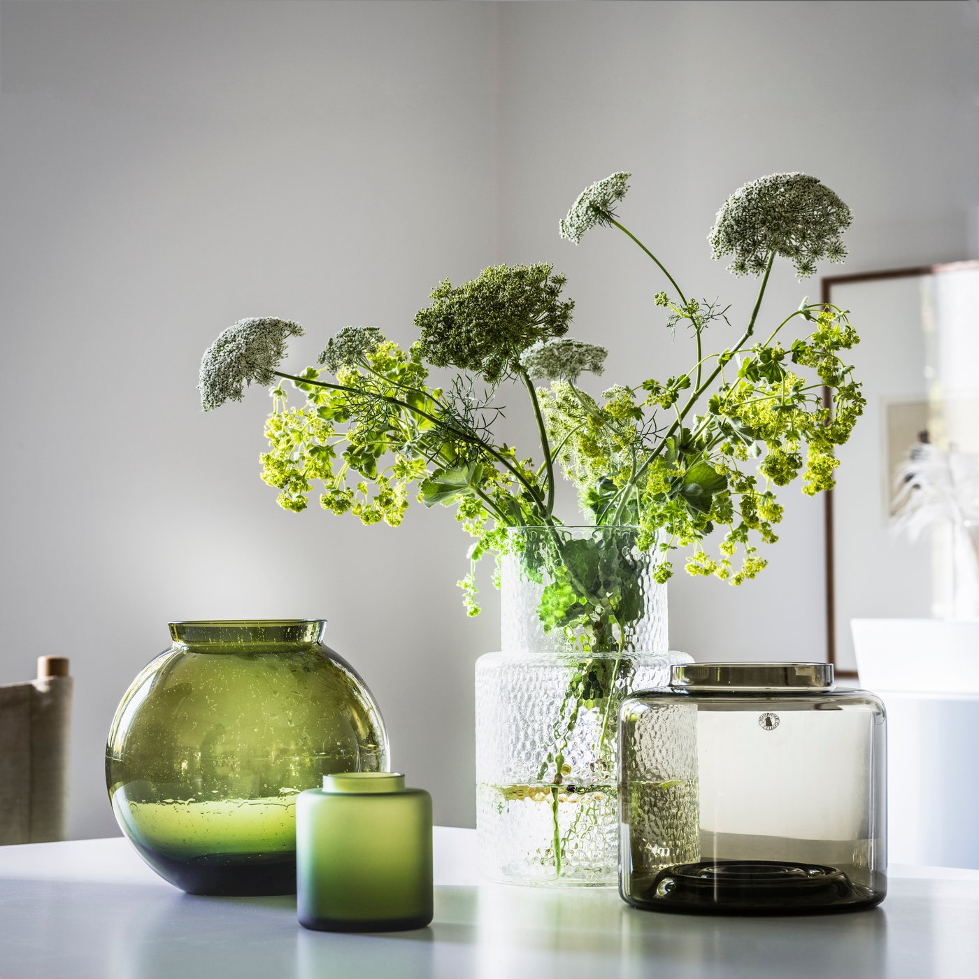 Verschillende soorten KONSTFULL vazren met bloemen erin staan op een witte tafel in de woonkamer.