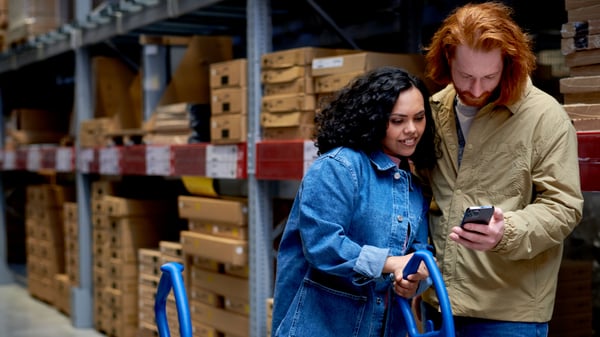 A couple shopping in the IKEA wareouse, looking at their phone