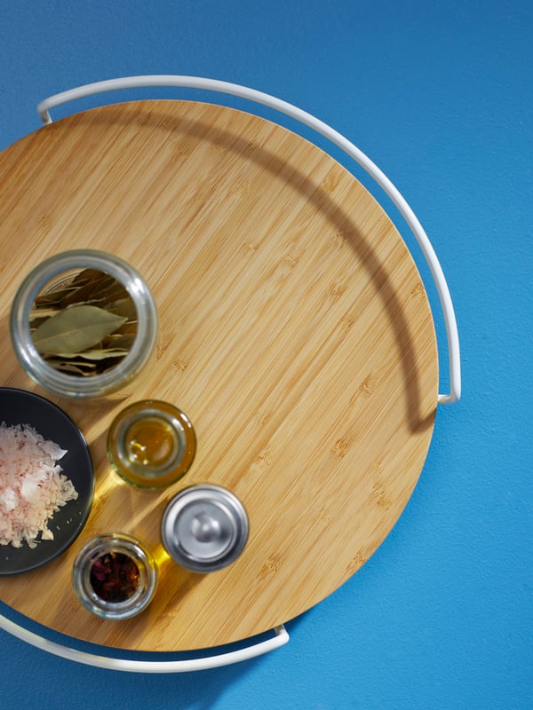 An APTITLIG lazy susan, made from bamboo, with salt, herbs, and condiments, against a bright blue background.