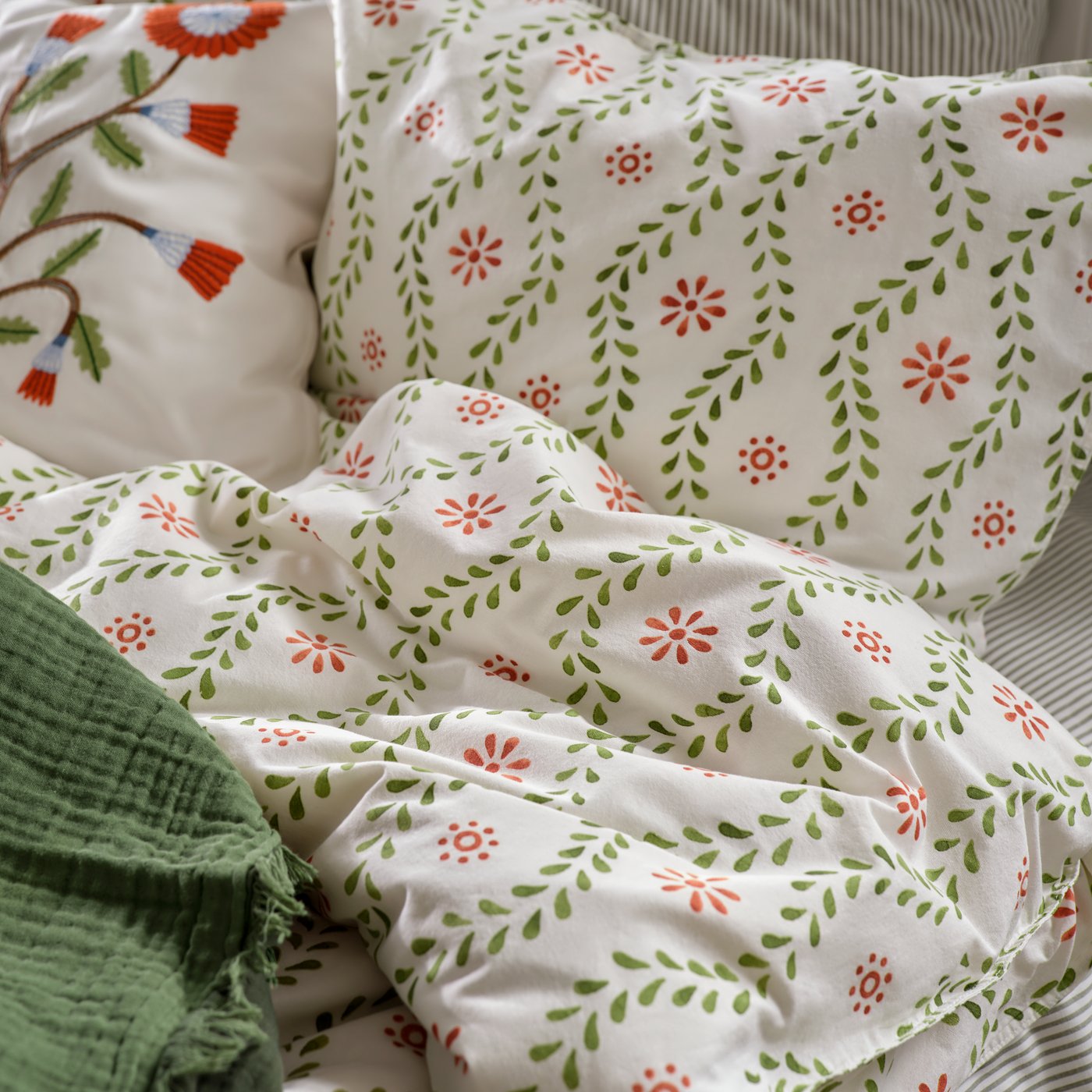 A close-up of a white/floral pattern FYRISVIDE duvet cover and pillowcases, embroidered cushion cover and throw on a bed.