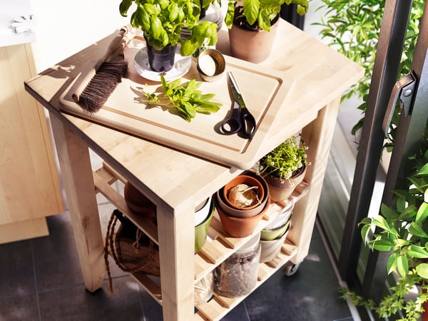 A wooden BEKVÄM kitchen trolley with a wooden chopping board with fresh herbs in the kitchen.