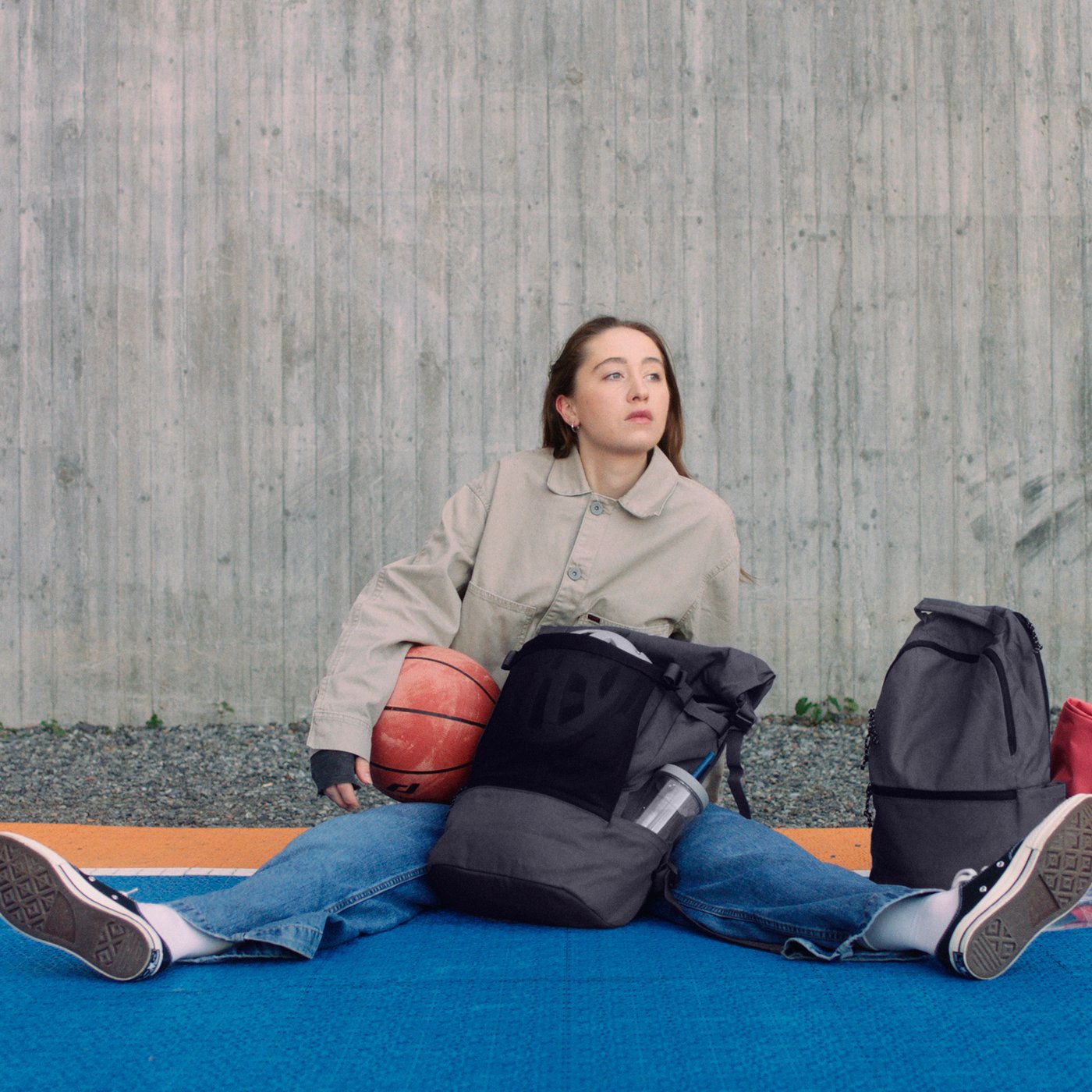 Eine Person sitzt mit einem Basketball unter dem Arm auf einem Basketballplatz, umgeben von verschiedenen IKEA Taschen.