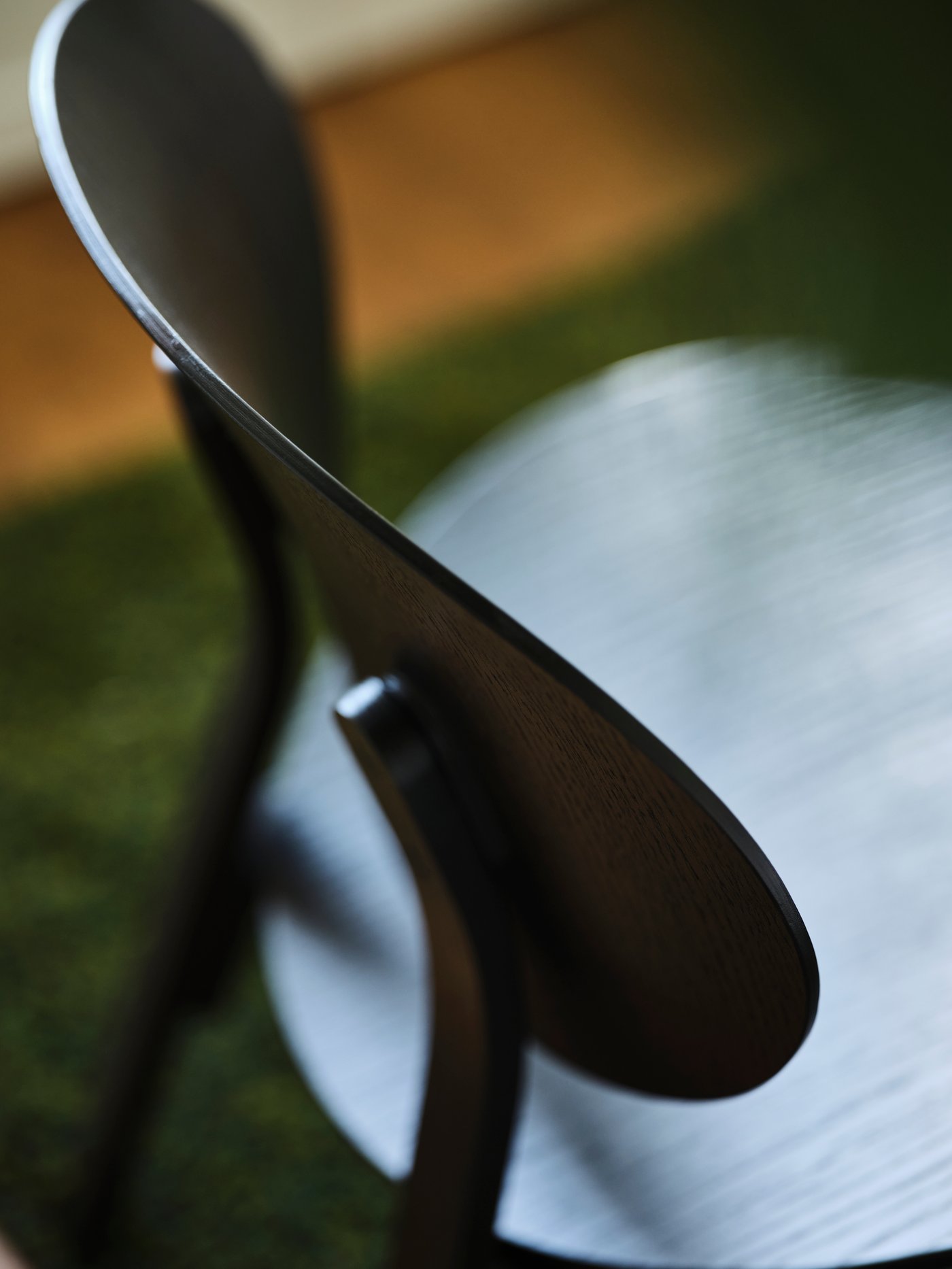 A black stained oak veneer FRÖSET easy chair on a dark green carpet.