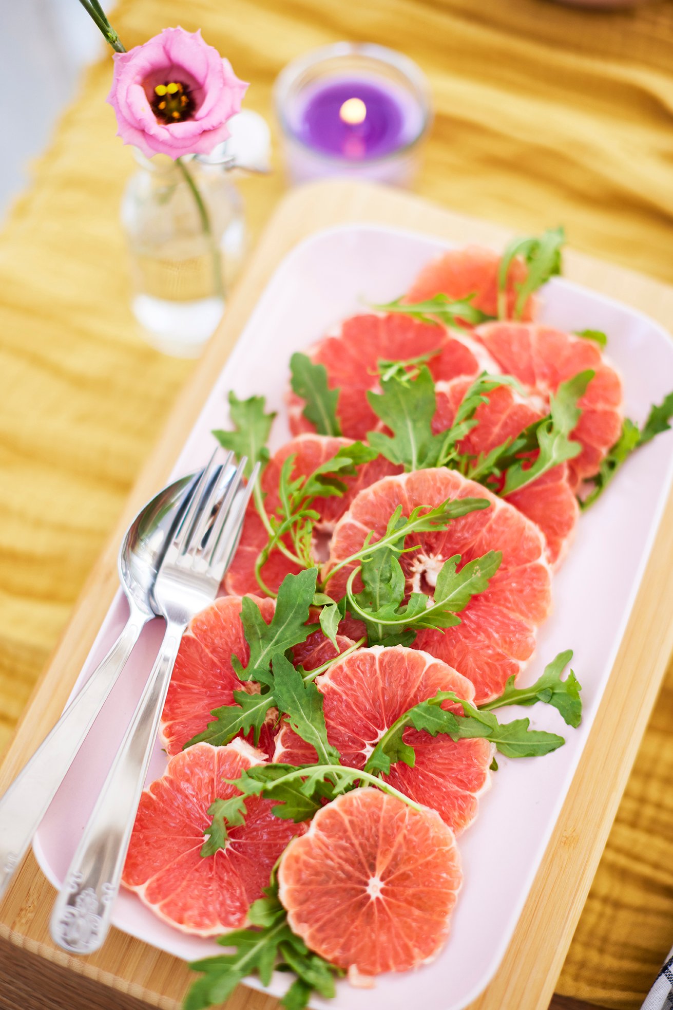 A rectangular serving dish with grapefruit slices and rocket leaves on a wooden board