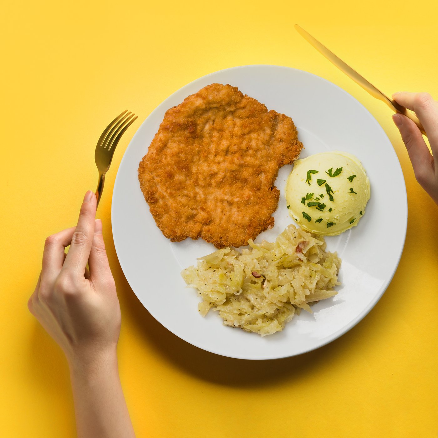 Kotel schabowy na talerzu z ziemniakami puree i kapustą zasmażaną.