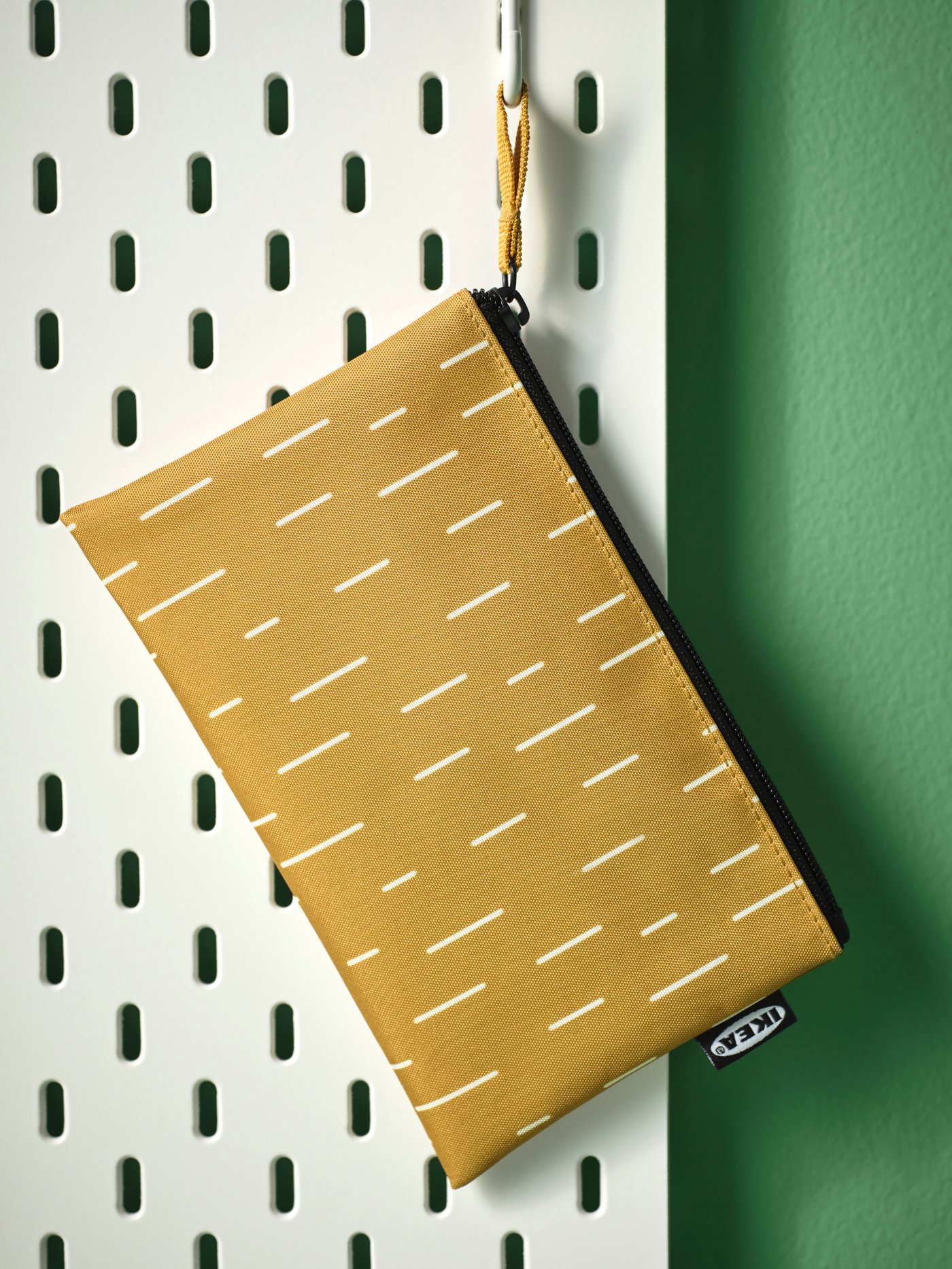 Sivomodra SKYNKE torba visi na kavlju na beli SKÅDIS perforirani plošči, pritrjeni na zeleno steno.