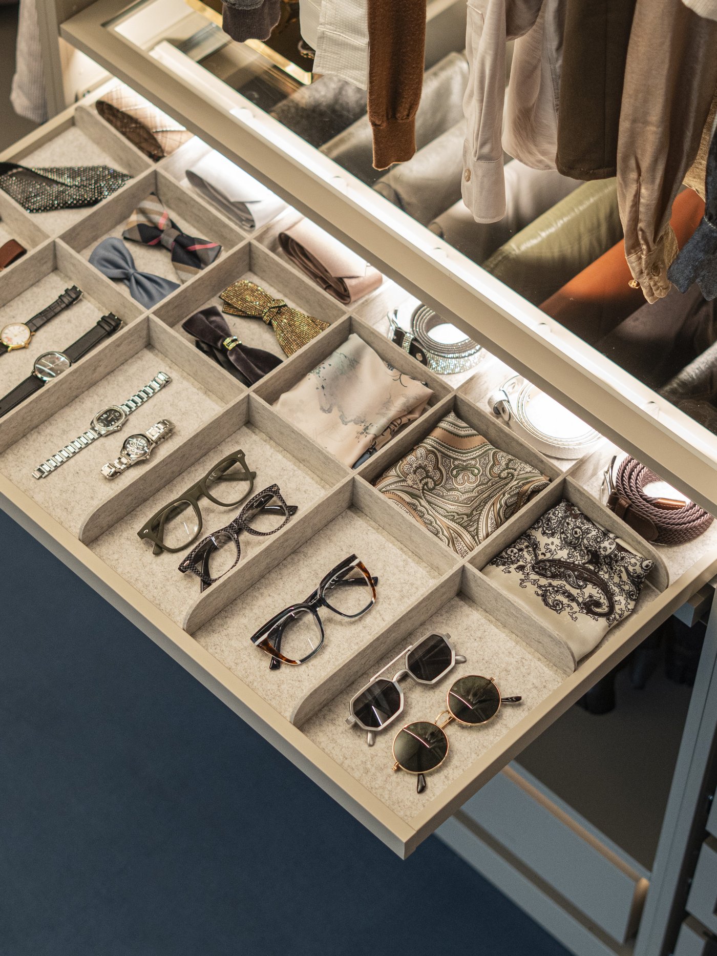 Vassoio estraibile bianco KOMPLEMENT all’interno di un armadio, organizzato con occhiali, orologi e accessori in scomparti separati.