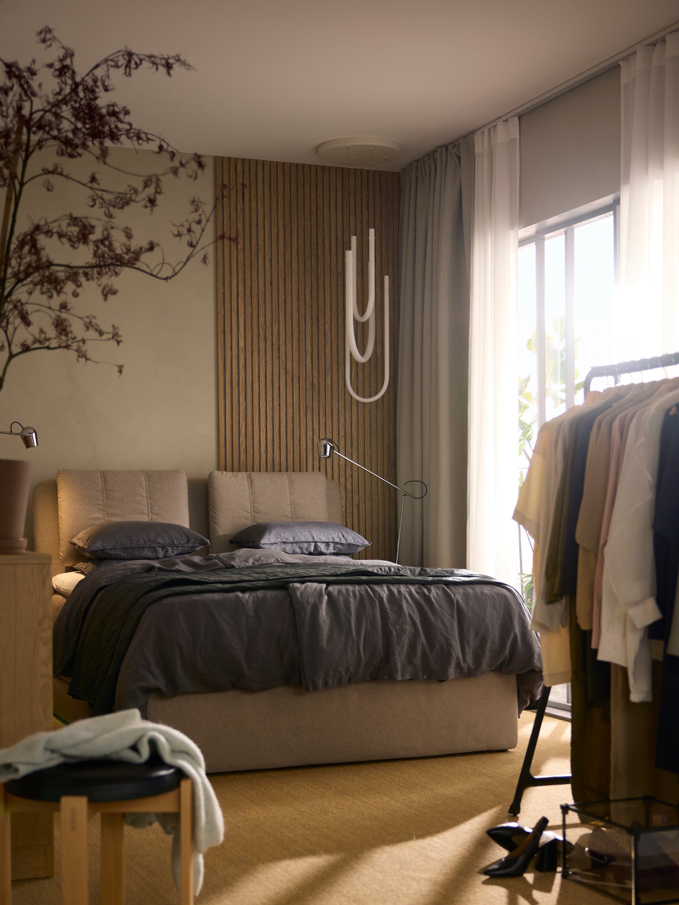 A beige LILLFJÄLLET upholstered bed with storage covered with dark grey DYTÅG bed linen with a VARMBLIXT LED lamp above it.