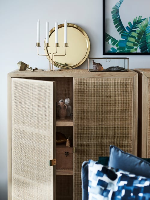 On top of a wooden cabinet is a brass-colour GLATTIS tray leaning against the wall, by a metal candelabra and gold decor.