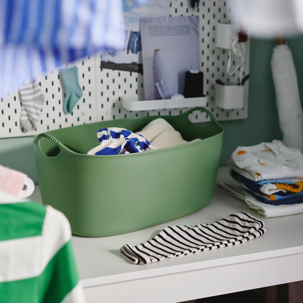 A 35-liter green, indoor/outdoor TORKIS flexi laundry basket holds clothes on a white surface where clothes are being folded.