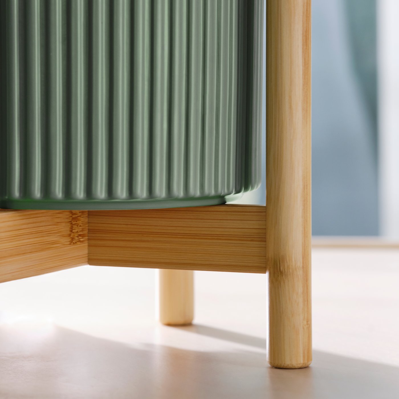Dettaglio del portapiante DAKSJUS in bambù chiaro con vaso verde rigato appoggiato sulla struttura in legno.