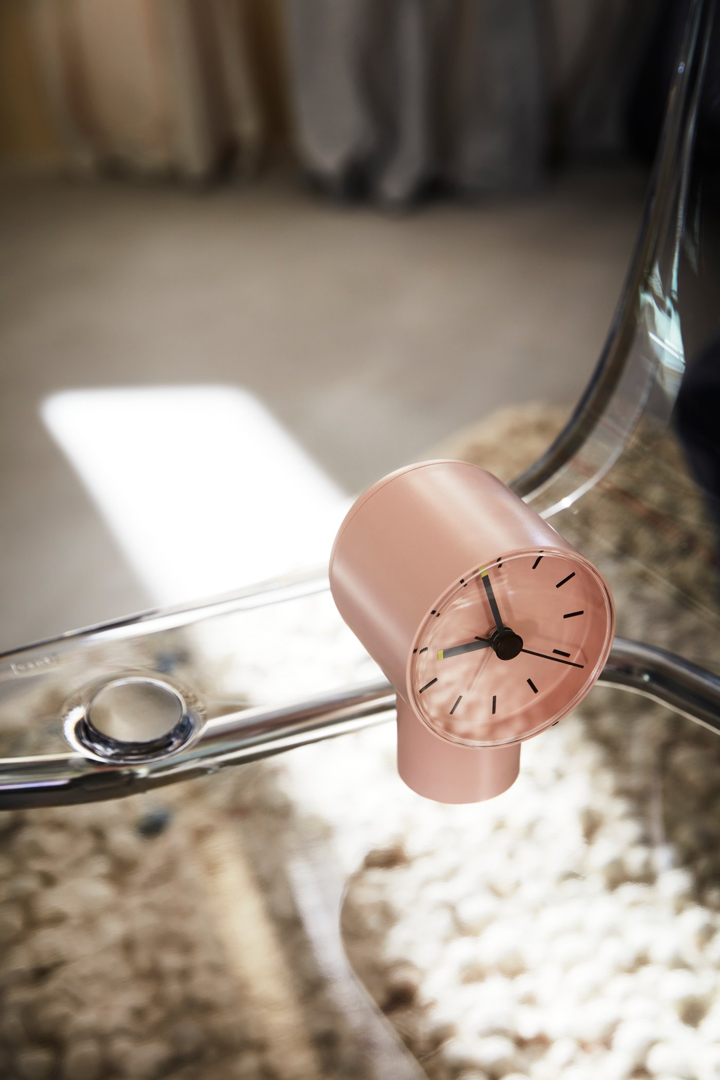 A light, dimly sunlit surface on which stands a pale-pink BONDTOLVAN analog alarm clock.