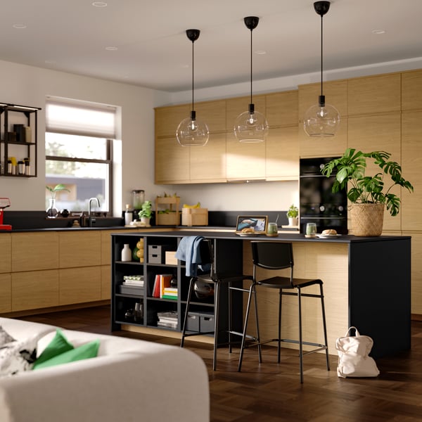 A dining room with VOXTORP oak effect drawer fronts and doors, three ceiling lamps hanging, wall frame shelves and chairs.