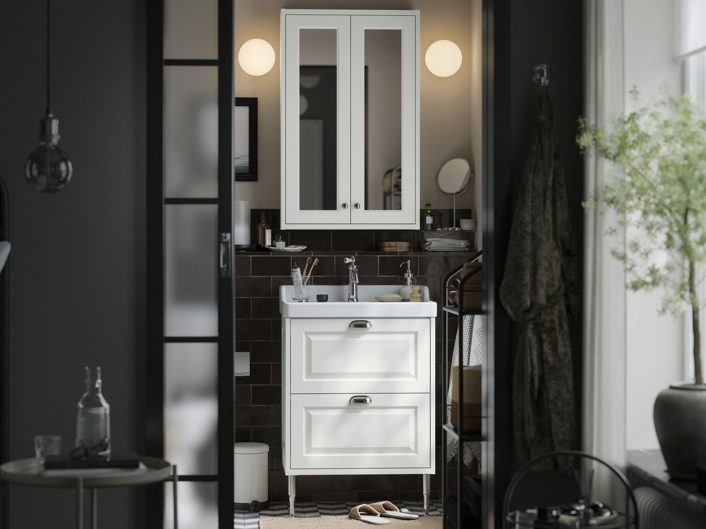 A small traditional style bathroom with white TÄNNFORSEN storage furniture, two soft round lamps and black details.
