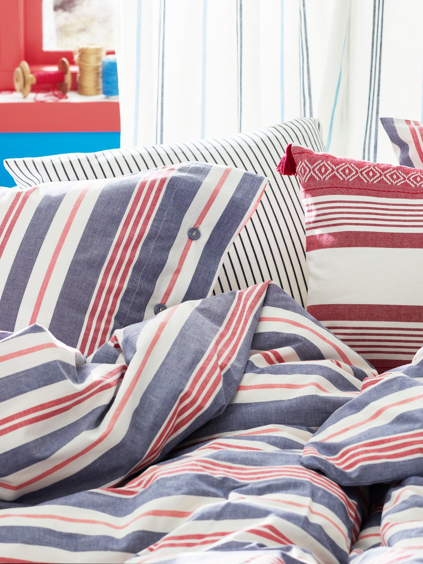 A white sofa with cushions and a blanket, a handwoven rug, a black side table with a vase and bowl, and a pendant above.