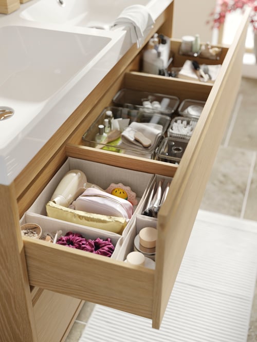 Close-up of the open drawer of an ÄNGSJÖN wash stand, containing toiletry items set in BOLLÖSUND drawer organisers.