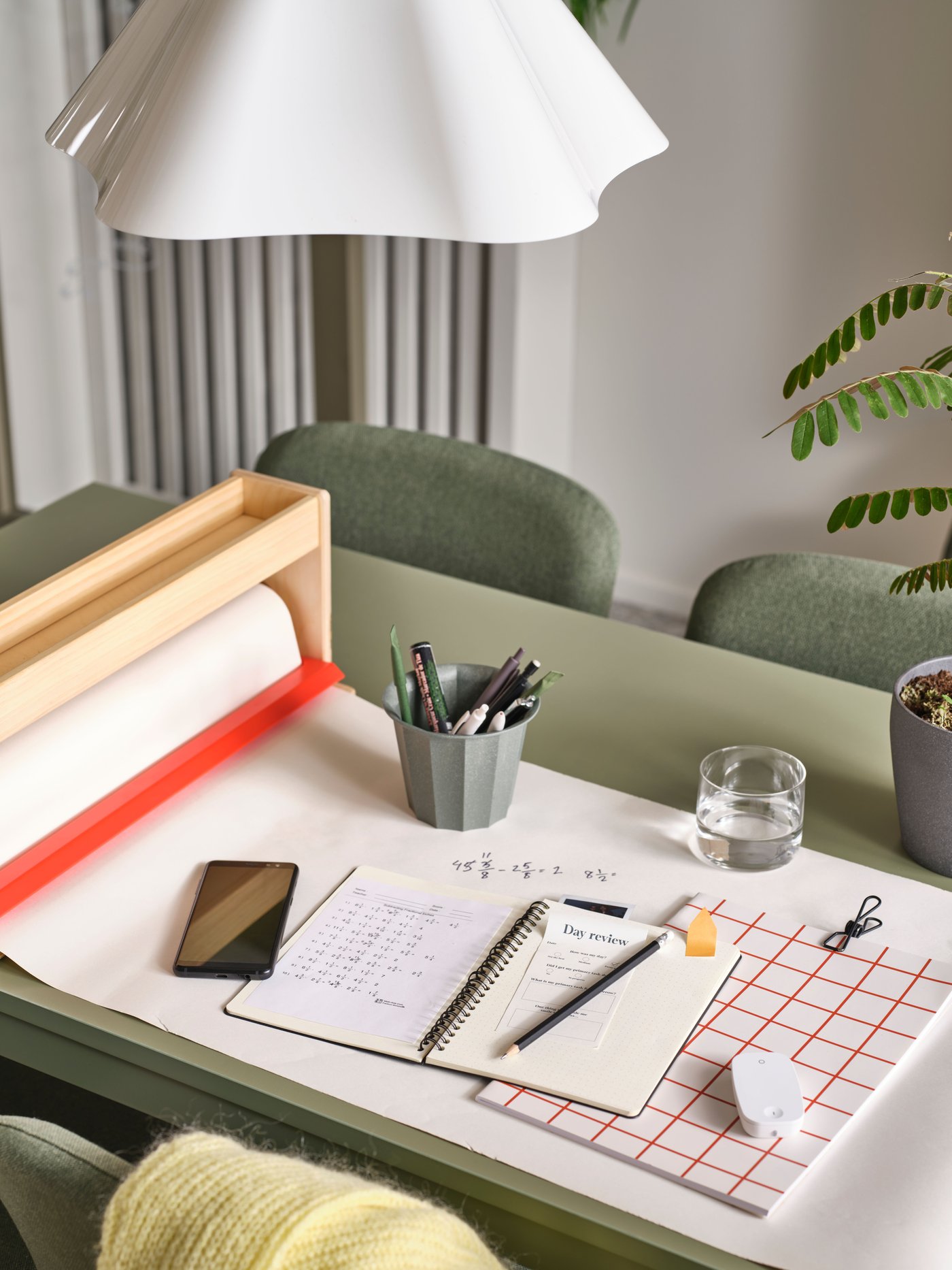 The wireless dimmer/power switch of a TRÅDFRI starter kit lies on a green table underneath a white ZEBRASÄV pendant lamp.