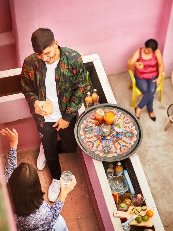 Dos personas onversando y bebiedo en un balcn. En el borde del balcón se ve la bandeja de la colección sosteniendo vasos llenos de líquido.