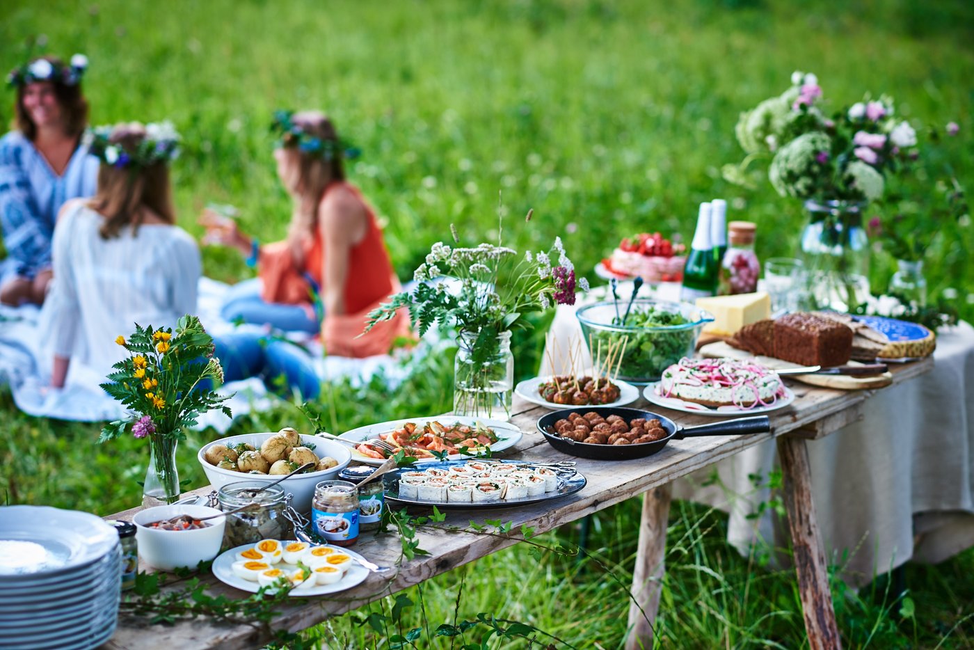 Frauen sitzen auf einer Wiese und feiern das schwedische Sommerfest Midsommar