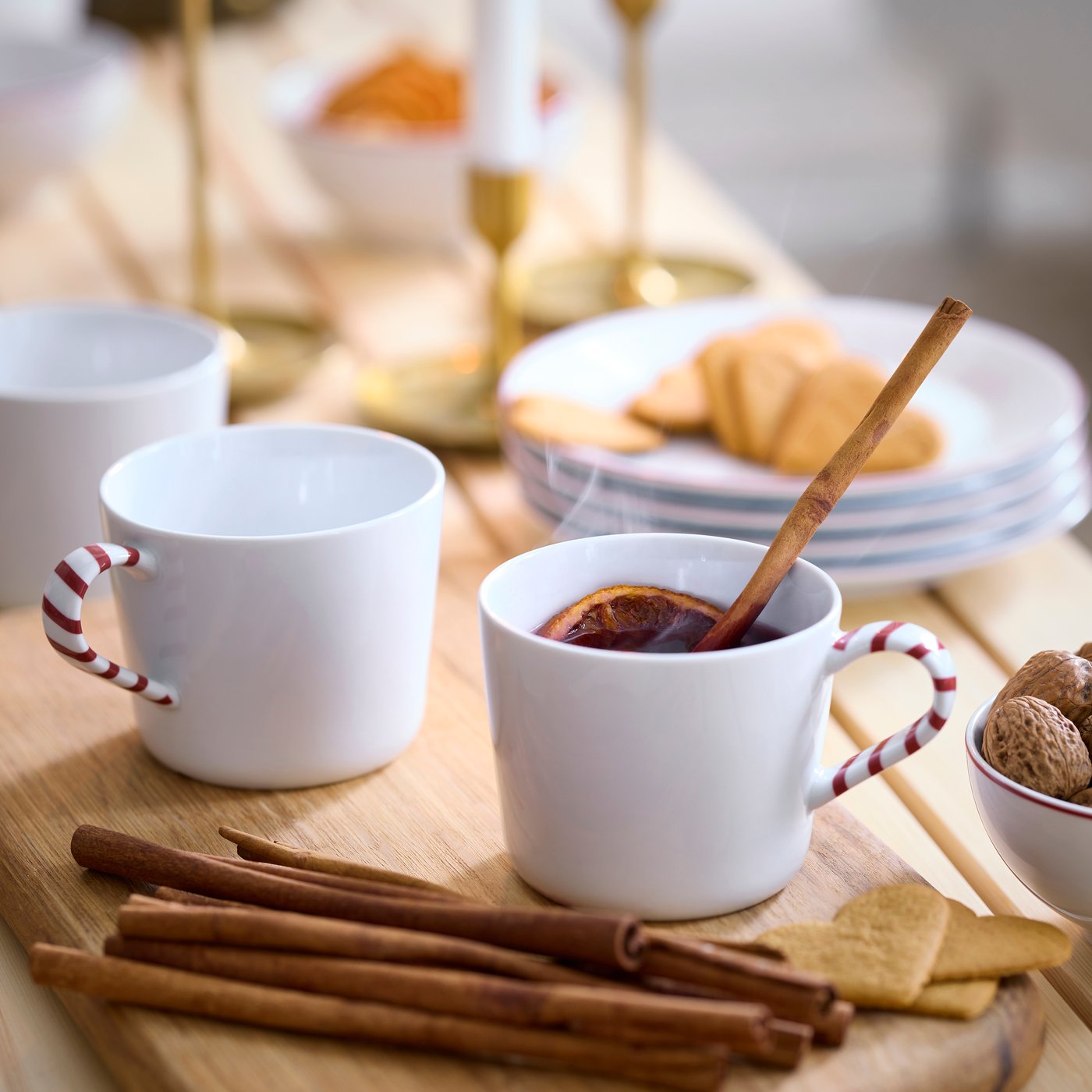 White VINTERFINT mugs sitting on a wooden board. Cinnamon sticks and cookies behind