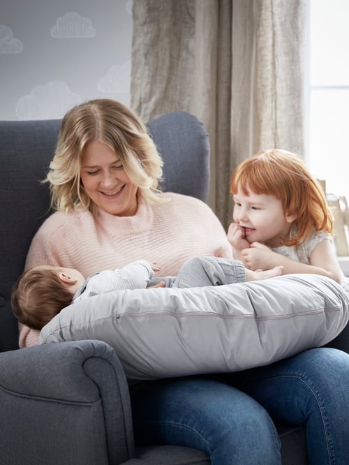 Une femme est assise sur un fauteuil STRANDMON. Elle tient un bébé sur un coussin LEN et une fillette se trouve à côté.