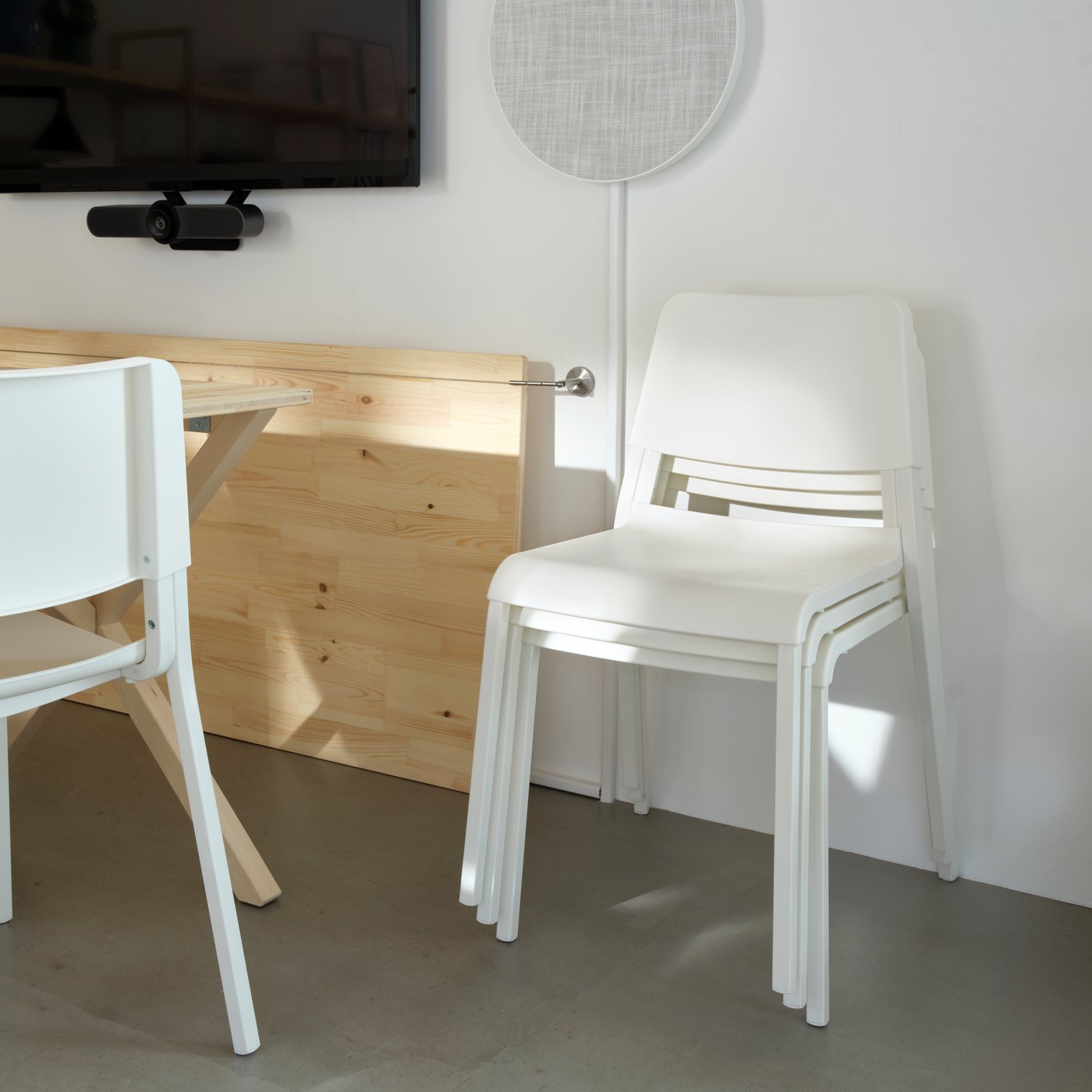 Close-up of three stacked chairs and a folded wooden table leaning against a white wall.