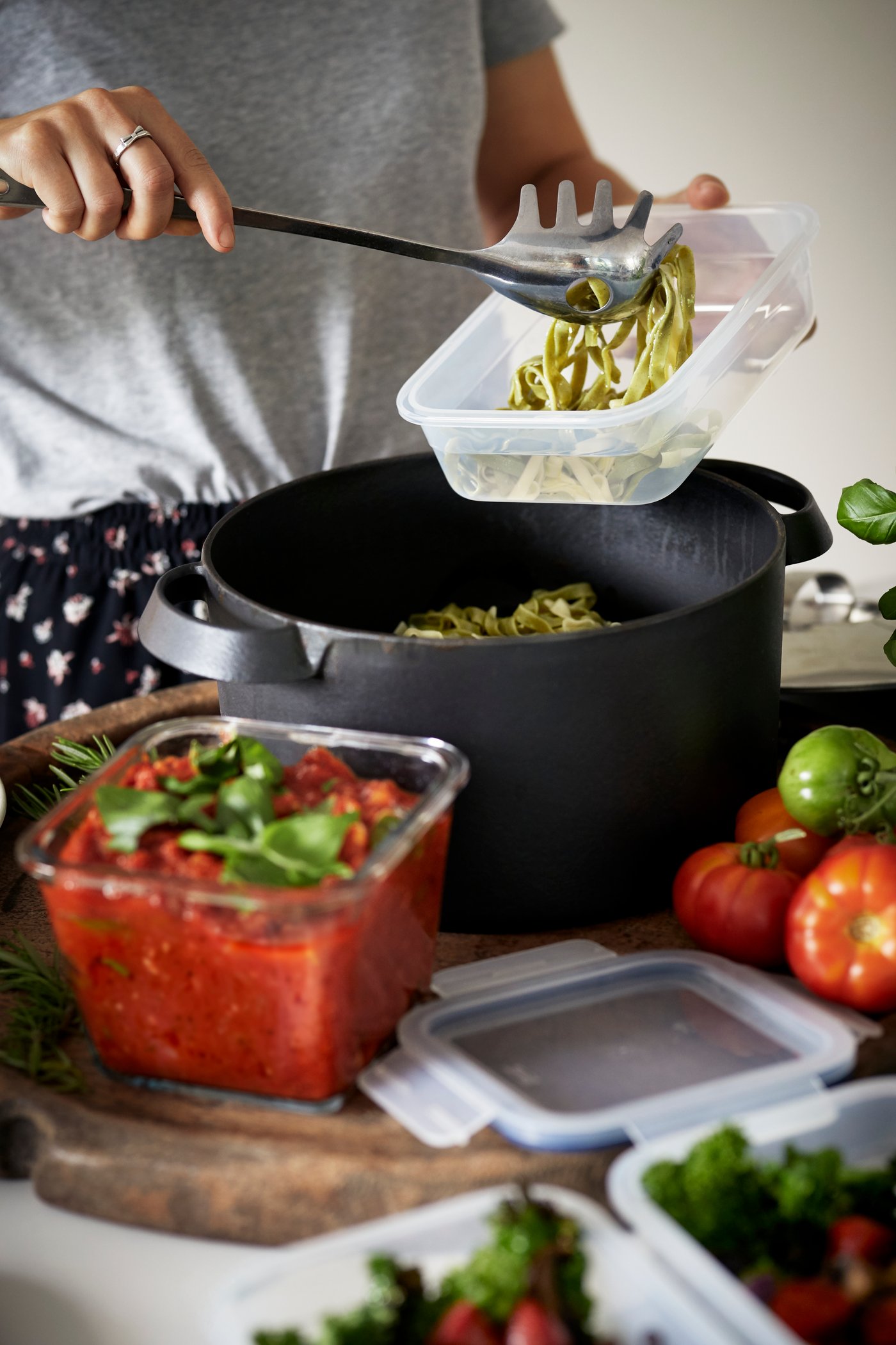 A kitchen setting shows a person using IKEA 365+ food containers to store freshly cooked pasta and tomato sauce.