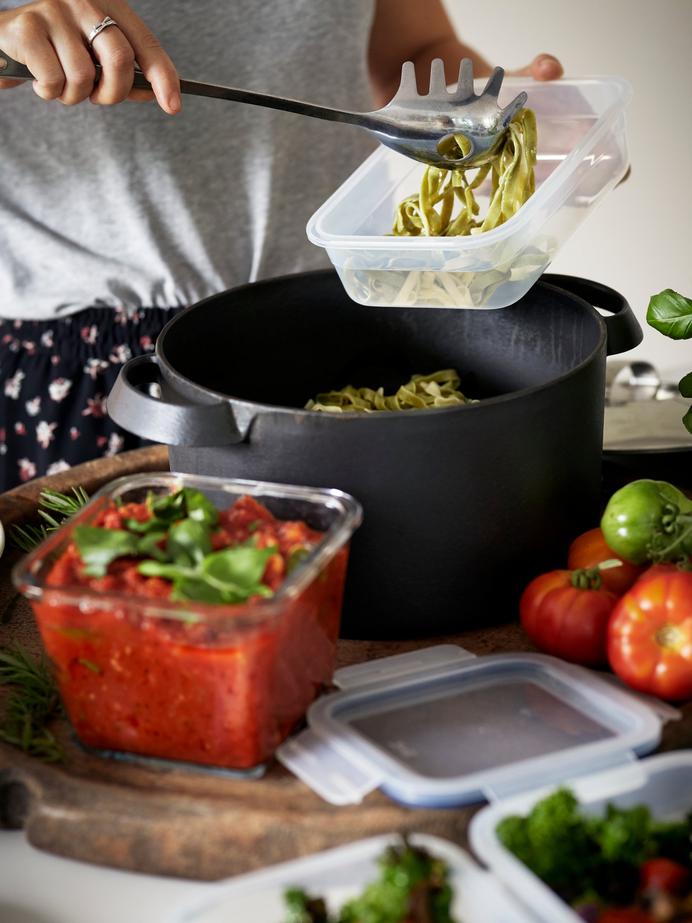 A kitchen setting shows a person using IKEA 365+ food containers to store freshly cooked pasta and tomato sauce.