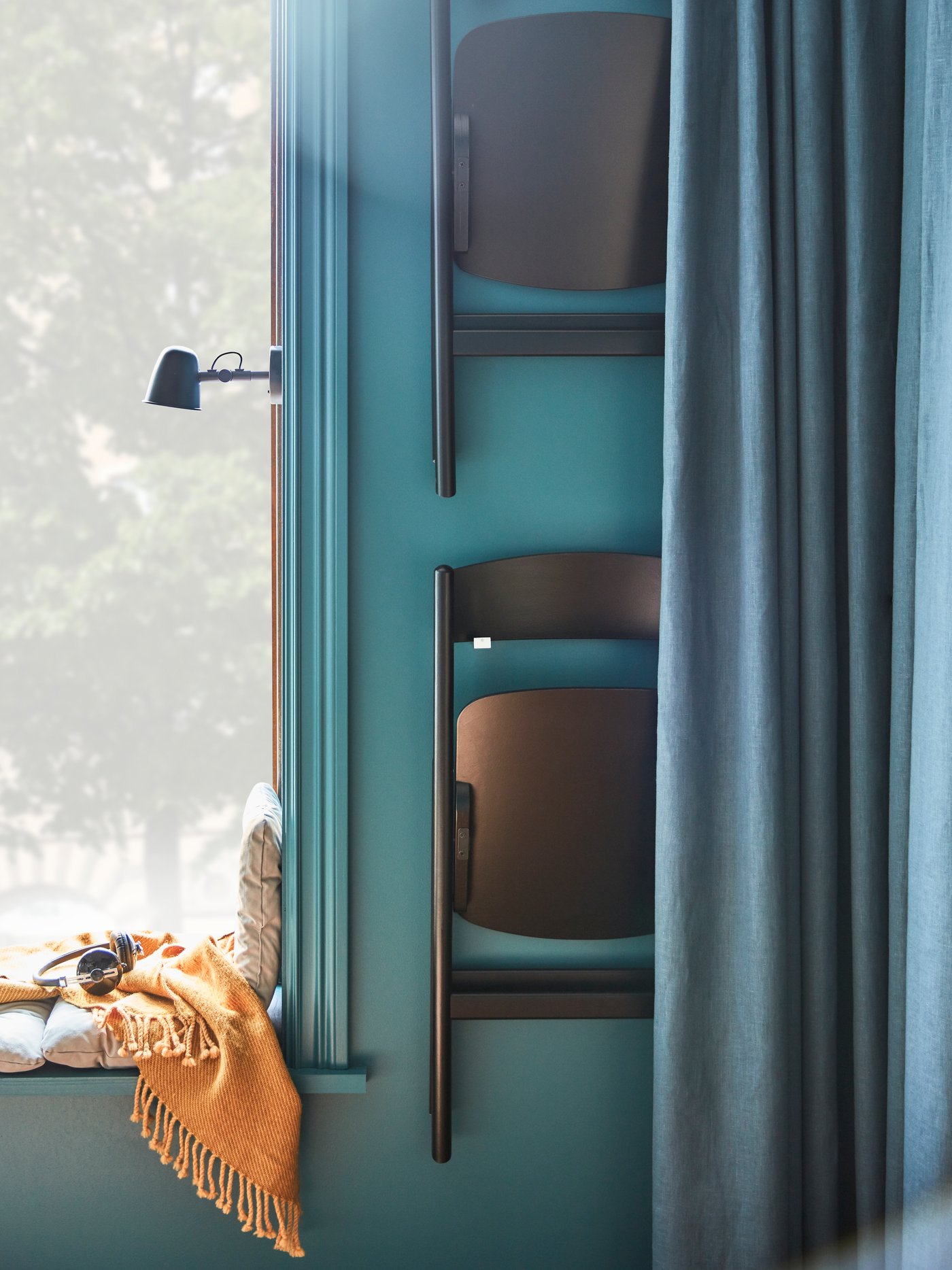 Two black folding chairs hang on wall-mounted hooks next to a window, and they are easily hidden by a blue curtain.