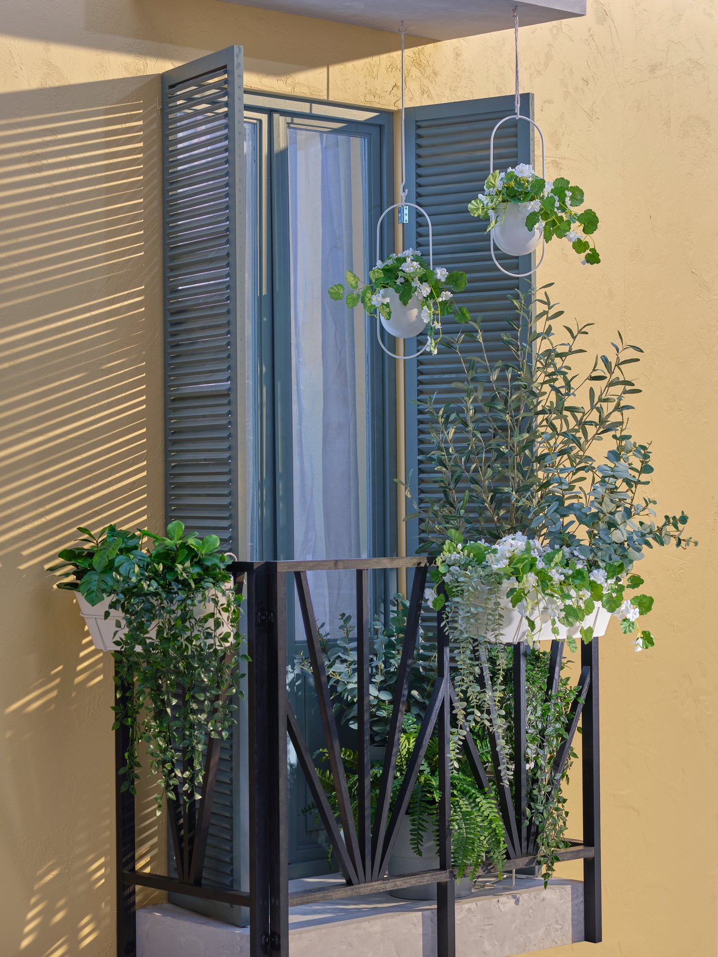 Plantas FEJKA en maceteros colgantes CHILISTRÅN y jardineras VITLÖK colgadas de las barandillas de hierro forjado negro de un balcón soleado.