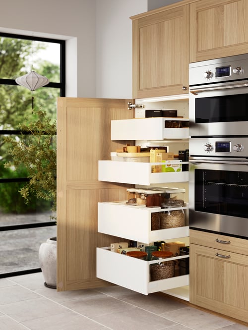 A high pantry with the door open and the drawers pulled out beside built-in kitchen appliances and more cabinets.
