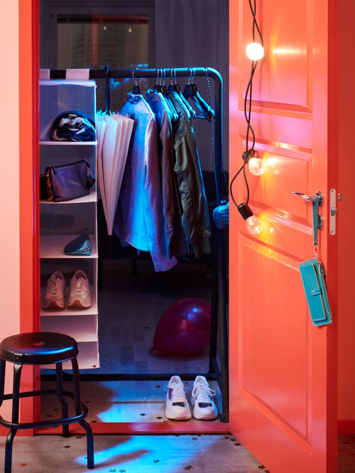 Hallway lit by lighting kit, red door with blue purse, stool, clothes rack with clothing items, storage with 6 compartments.