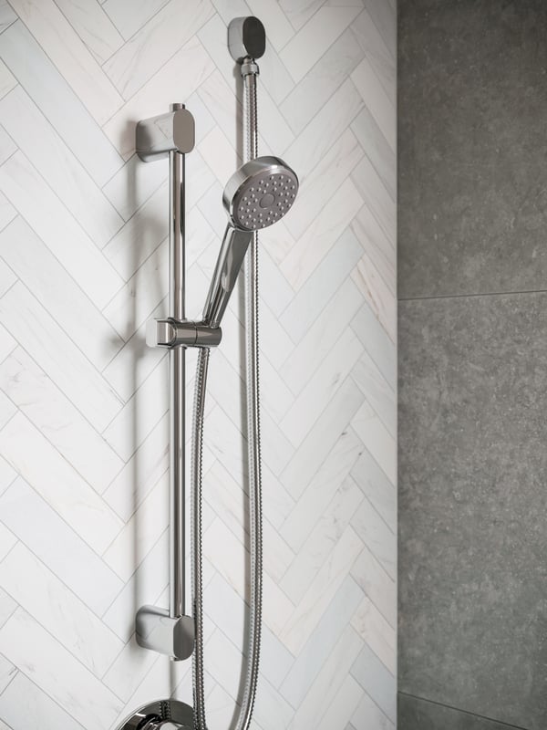 Une barre de douche BROGRUND est fixée sur un mur de douche et est accompagnée d’une douchette surmontée d’un mitigeur thermostatique BROGRUND chromé.